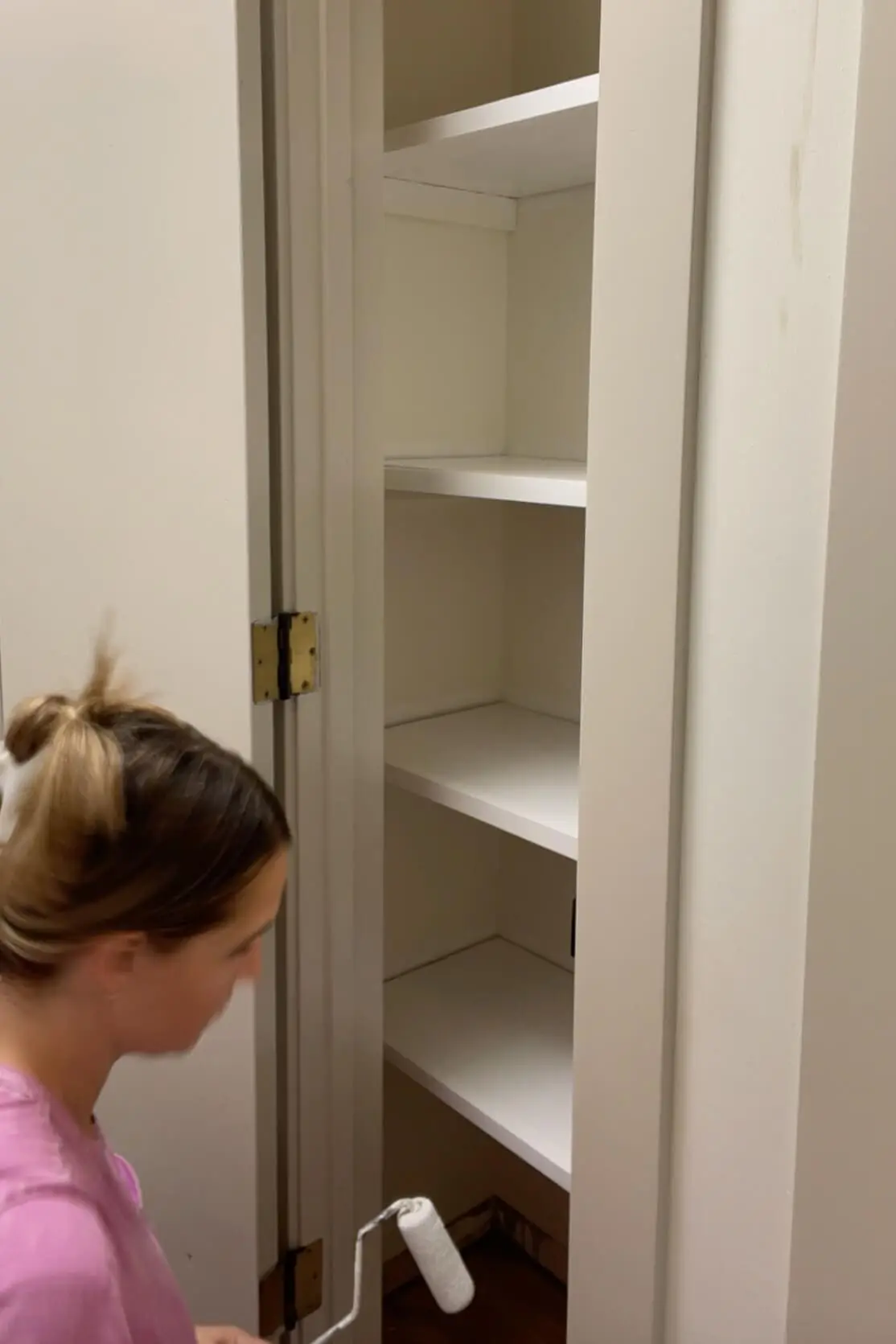 Woman applying white paint to freshly installed shelves in a linen closet for a clean and modern look.